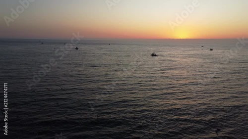 Aerial view of fishing boats sailing at sunset with a flock of sea birds flying over the ocean