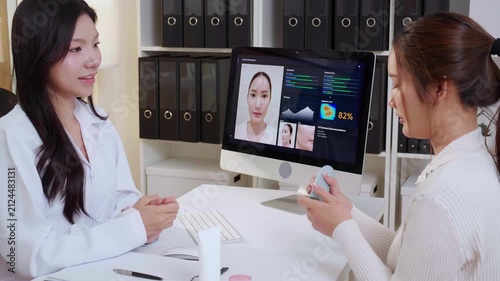 Asian woman doctor explaining skincare cream product for young female patient in clinic, professional dermatologist showing ai skin analysis on computer screen, medical face beauty care consult.