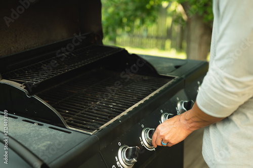 Person turning on a gas grill before grilling burgers at a backyard barbecue