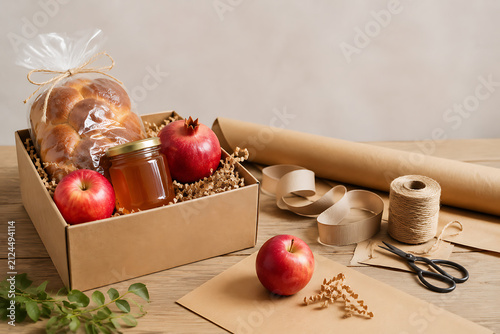 Rosh Hashanah gift wrapping station with honey jar, apples, wrapped challah, pomegranate, kraft paper and rib…

