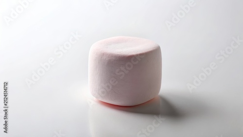 A single, softly-lit, pale pink marshmallow rests on a pristine white surface