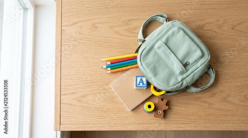 Mint green kids backpack spilling school supplies and toys on wooden desk top view