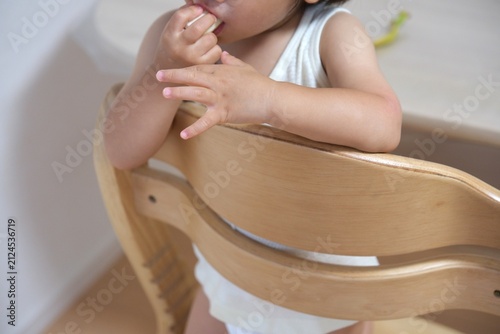 Close-up of a toddler eating a banana with both hands on a wooden chair
