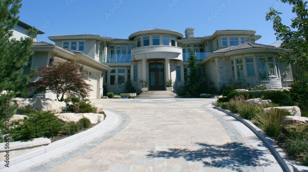 Obraz premium Stunning modern mansion with large driveway, landscaped garden, and clear blue sky, showcasing luxurious architecture and inviting entrance