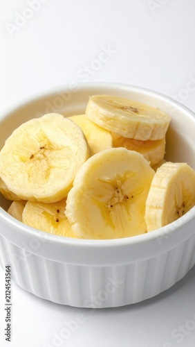 Sliced ripe bananas fill a white ramekin on a bright background