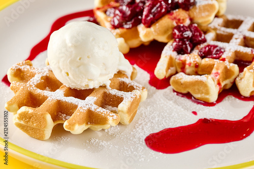 Golden Belgian waffle with creamy ice cream, juicy cherry topping and glossy red sauce for a colorful dessert menu