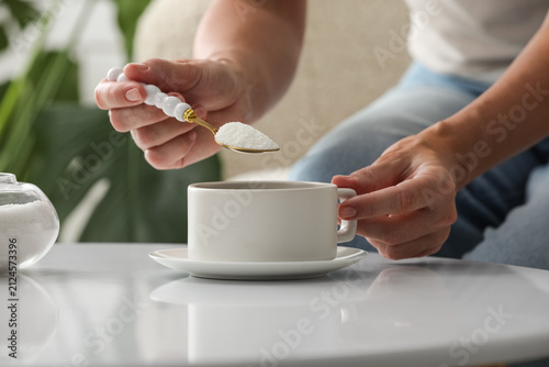 Foto Woman adding white sugar to a cup of coffee or tea, sweetening beverage, unhealt