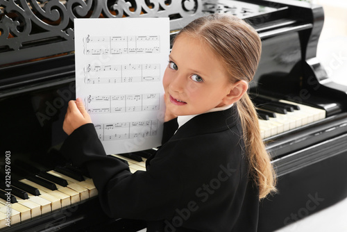 Cute little happy girl in school uniform with notes playing grand piano at mu...