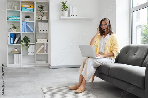 Female technical support agent working with laptop on sofa in office
