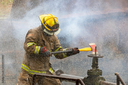 Bild auf Leinwand Firefighter in fireproof clothe is holding axe to destroy the water valve near b