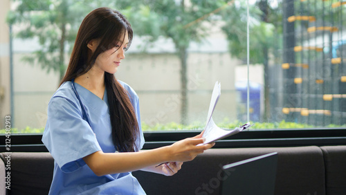 Doctor working on laptop and reviewing documents in medical office. Medical professional in office, using laptop and reviewing documents. Female doctor in healthcare workplace, patient care.