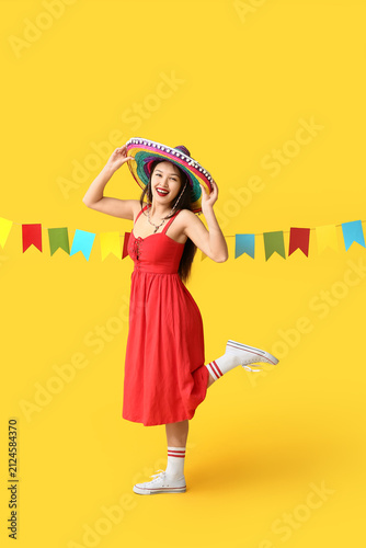 Happy young woman in Mexican sombrero hat and with garland on yellow background