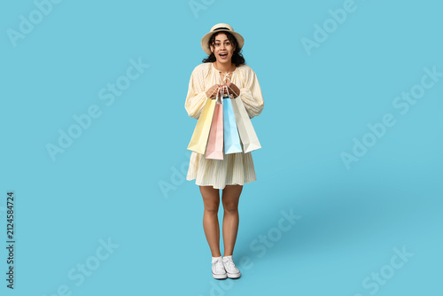 Pretty African-American woman with shopping bags on blue background