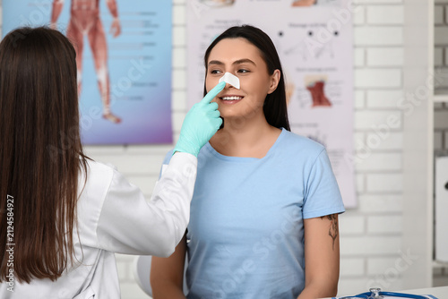 Plastic surgeon and happy young woman with bandaged nose in clinic