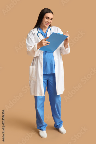 Beautiful young pregnant doctor with clipboard on brown background
