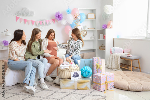 Young pregnant woman with her friends sitting at baby shower party in bedroom
