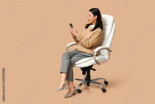Portrait of young Asian businesswoman with mobile phone sitting on armchair a...