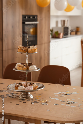 Stand with confectionery and confetti on dining table in kitchen decorated fo...