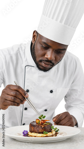 Professional Black male chef plating gourmet steak with tweezers