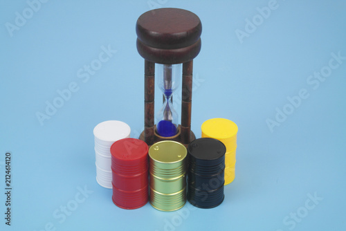 Different crude oil barrels and hourglass on blue background.