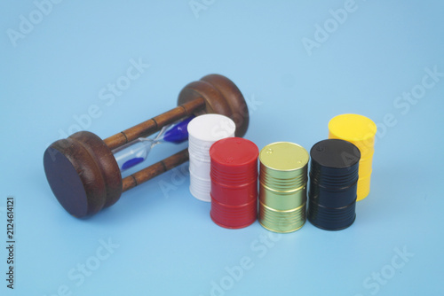 Different crude oil barrels and hourglass on blue background.