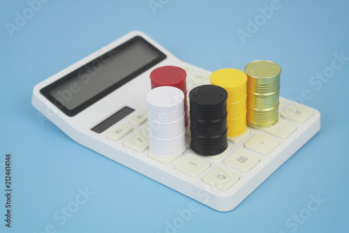 Different crude oil barrels on calculator on blue background. Crude oil price concept.