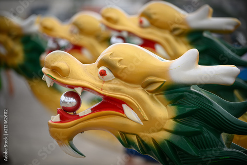 A close-up of ornate dragon boat figureheads lined up in a row, showcasing their vibrant gold, green, red, and white colors