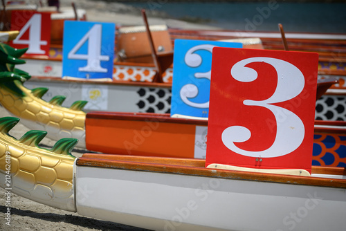 A dragon boat marked with the number 3 is lined up alongside other racing boats before a competition or practice session