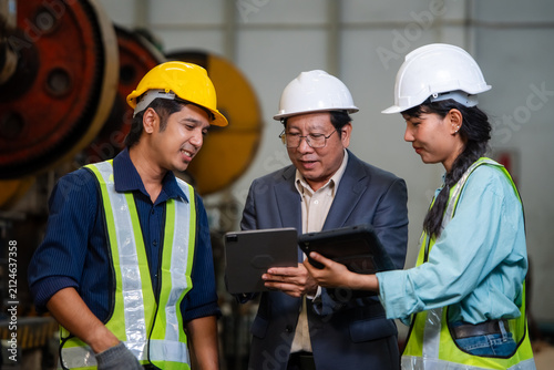 Senior factory manager and diverse engineering team discussing production data on digital tablet for quality control and industrial manufacturing business development in modern plant.