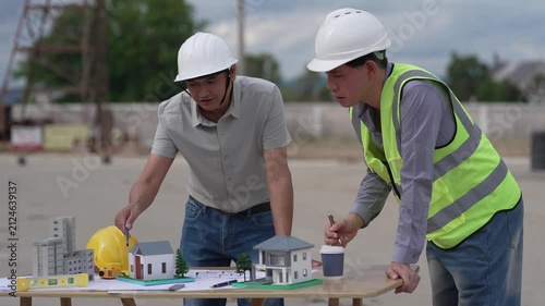 Architect and Civil Engineer Discussing Building Plans with Architectural Models and Blueprint on Worktable