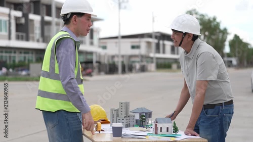 Architect and Civil Engineer Discussing Building Plans with Architectural Models and Blueprint on Worktable