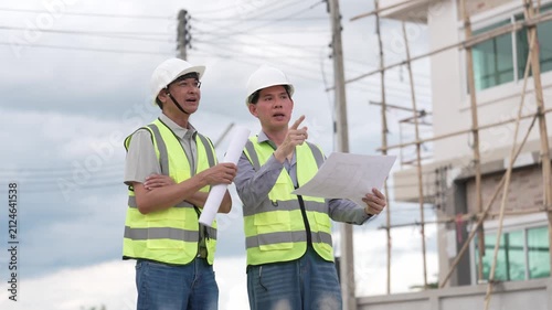 Two Civil Engineers in Hard Hats and Safety Vests Inspecting Construction Site with Blueprint