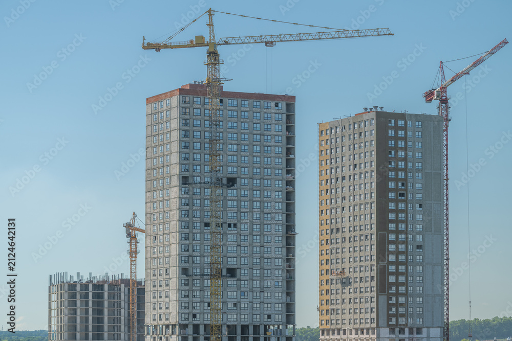 Fototapeta premium Construction of tall buildings with cranes on site in a city during bright daylight