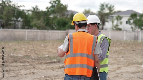 Two Civil Engineers in Hard Hats and Safety Vests Inspecting Construction Site with Blueprint