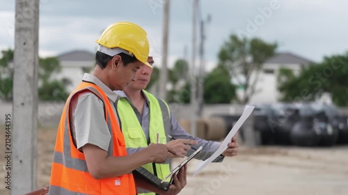 Two Civil Engineers in Hard Hats and Safety Vests Inspecting Construction Site with Blueprint