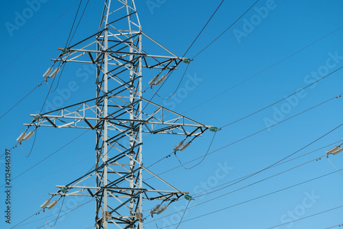 Steel transmission tower with multiple power lines against clear blue sky, detailed lattice framework, crossarms, ceramic insulators, and taut conductors, with transmission, tower, powerline, pylon