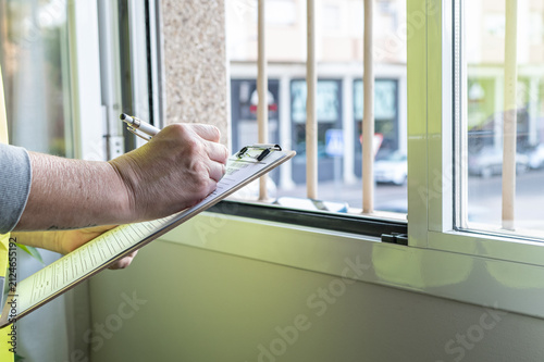 Professional inspector examining a window and writing notes on a clipboard, performing a thorough property assessment during a real estate inspection