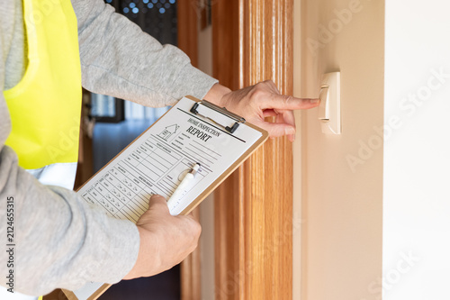 Home inspector conducting a thorough property assessment, reviewing a checklist on a clipboard while testing an electrical light switch in a residential house