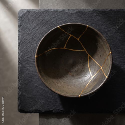 Broken ceramic bowl mended with gold lacquer kintsugi technique on slate background minimalist dark fine art concept for resilience healing recovery philosophy