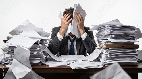 Stressed exhausted businessman overwhelmed by massive pile of messy paperwork and documents on desk