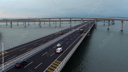 Aerial drone view of Qingdao Bay Cross-sea Bridge during blue hour dusk, heavy cargo trucks and vehicles driving on marine viaduct, grand Chinese transportation infrastructure