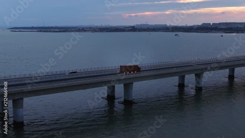 Evening twilight drone shot of Qingdao cross-sea highway, moving traffic and logistics trucks on giant bay bridge, landmark coastal infrastructure of Shandong China