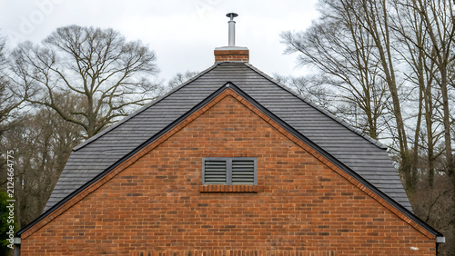Traditional brick house with chimney and dormer window. Classic red-brick cottage exterior featuring rooftop details and architectural charm.