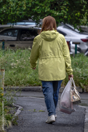 A woman with shopping is walking along the sidewalk on a summer day