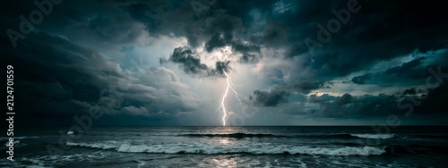 A powerful bolt of lightning strikes down towards the dark ocean waves during a dramatic thunderstorm at night, with heavy grey clouds filling the sky and a bright flash illuminating the horizon