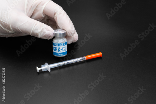 Gloved Hand Holding GHK-CU Peptide Vial with Insulin Syringe on Black Background