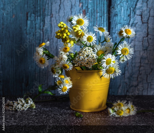 A small bouquet of meadow daisies in a small yellow bucket on a dark background.