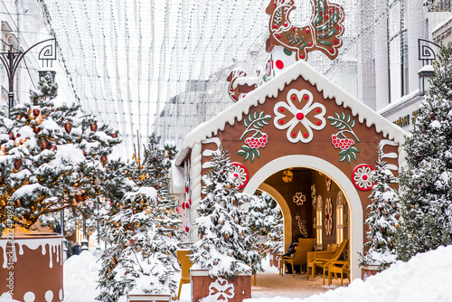 A gingerbread house with a sign among snow‑covered Christmas trees in Kamergersky Lane in Moscow. Concept for the New Year 2027.