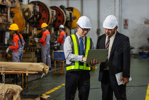 Factory Engineer Presenting Production Data to Business Executive Using Laptop in Manufacturing Plant