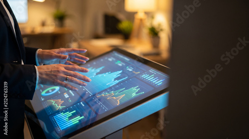 Businesswoman's Hands Gesturing Over Touchscreen Analytics Dashboard with KPI Graphs and Bar Charts in Modern Office